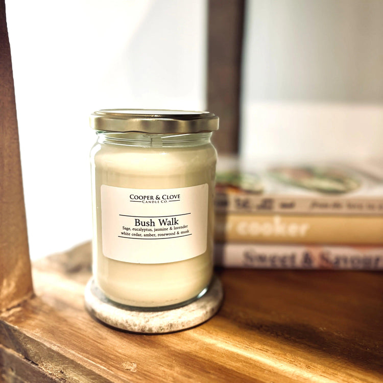 Bush Walk soy candle in glass jar with silver lid, featuring sage, eucalyptus & lavender notes, displayed on wooden shelf.