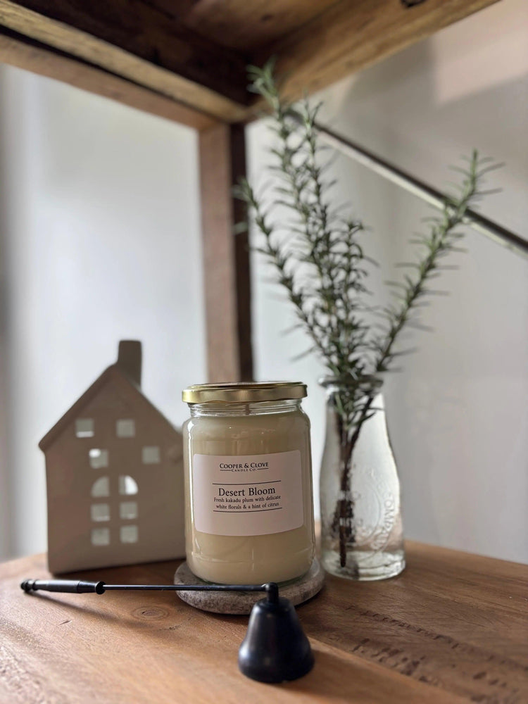 Desert Bloom luxury soy candle in glass jar with gold lid, styled on wood shelf with greenery and decor