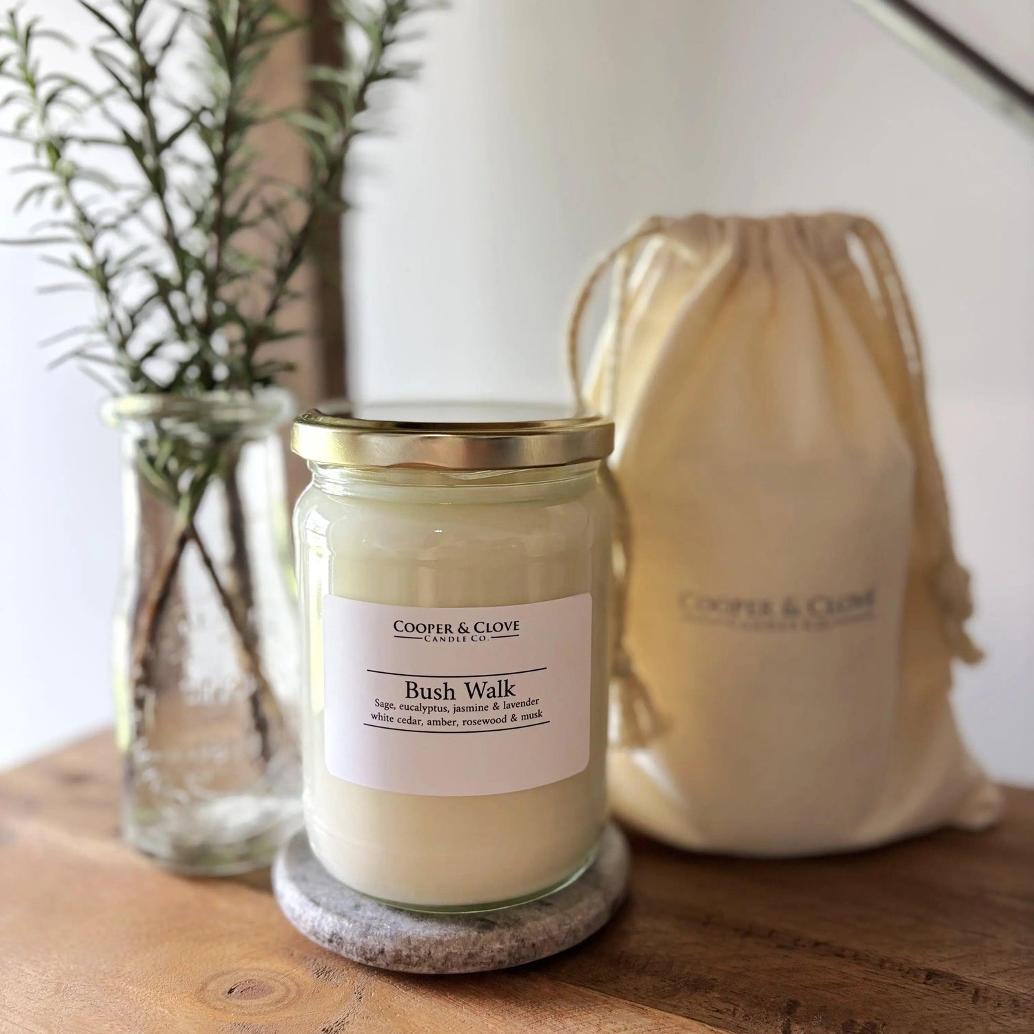 Bush Walk soy candle in glass jar with gold lid, minimalist label, beside linen drawstring bag and greenery