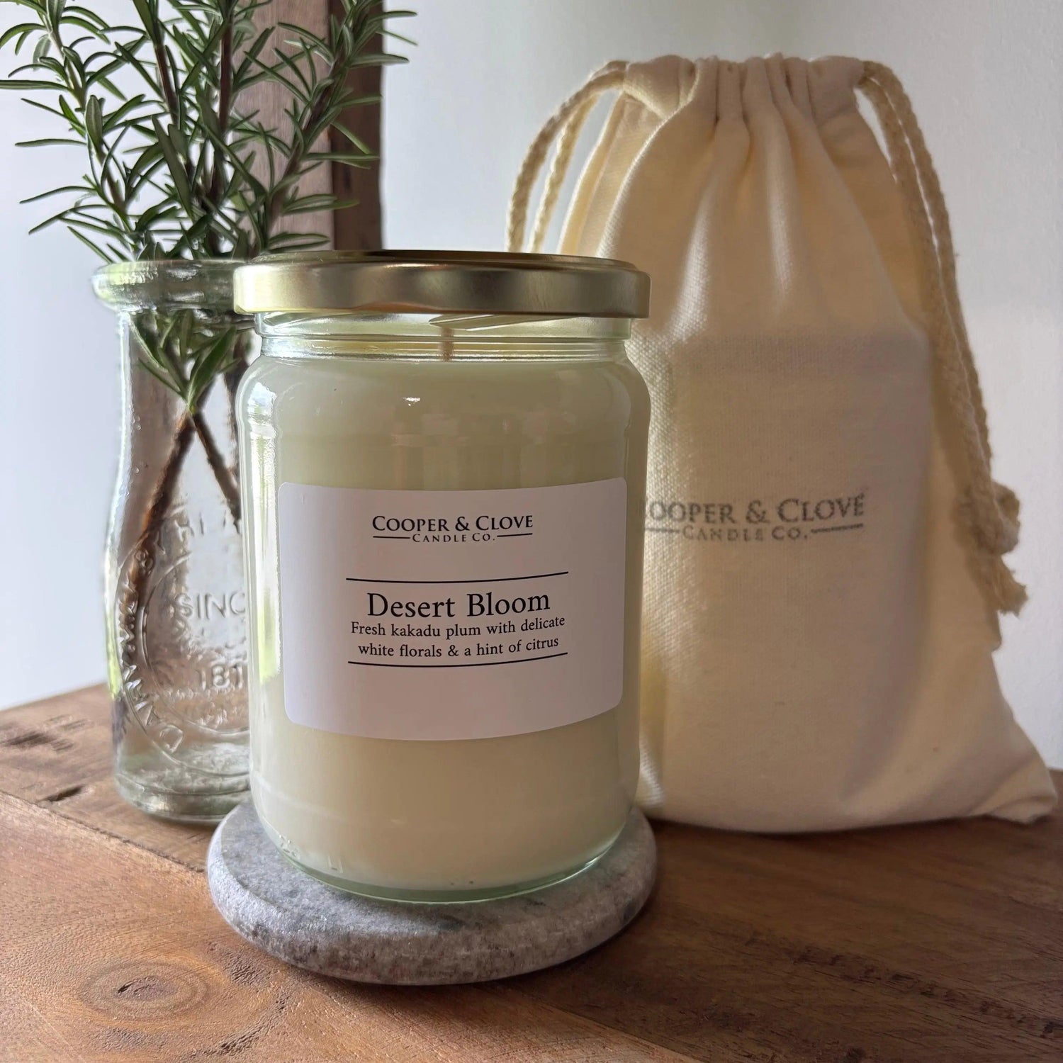 Desert Bloom soy candle in glass jar with gold lid, beside rosemary and drawstring bag, minimalist home fragrance