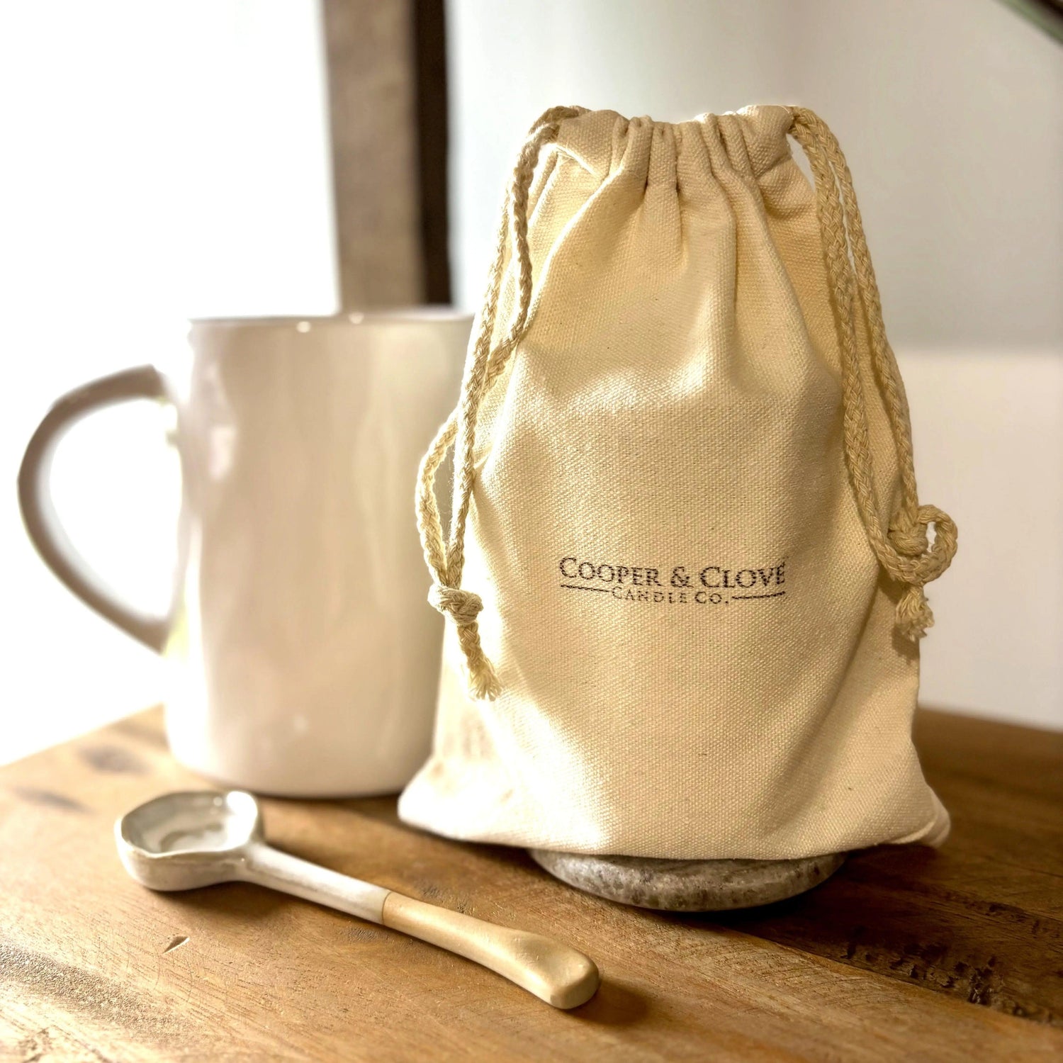 Cooper & Clove Candle Co. drawstring bag with ceramic mug and spoon on wooden table, minimalist home decor