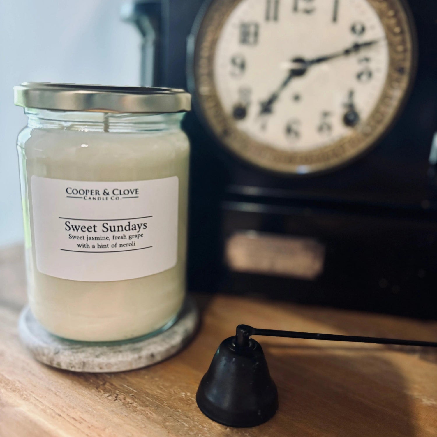 Sweet Sundays soy candle in glass jar with silver lid, jasmine grape scent, beside vintage clock on wood shelf