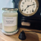 Sweet Sundays soy candle in glass jar with silver lid, jasmine grape scent, beside vintage clock on wood shelf