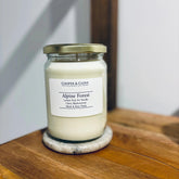 Alpine Forest soy candle in glass jar with gold lid, featuring lemon peel, fir needle, clove, blackcurrant, musk & rose petals scents