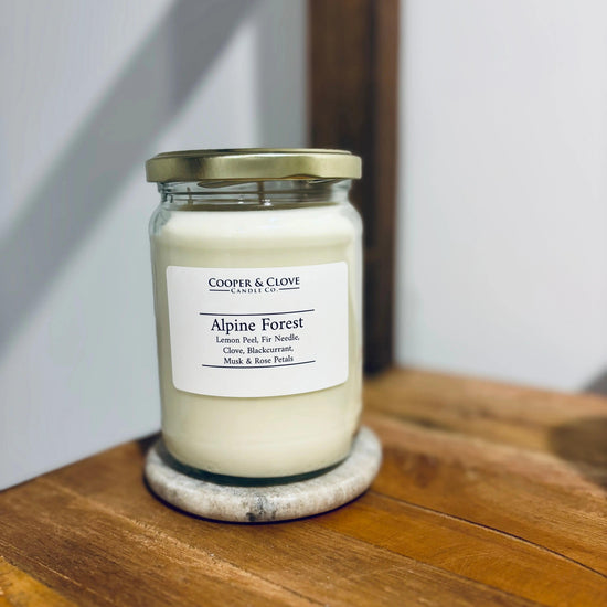 Alpine Forest soy candle in glass jar with gold lid, featuring lemon peel, fir needle, clove, blackcurrant, musk & rose petals scents