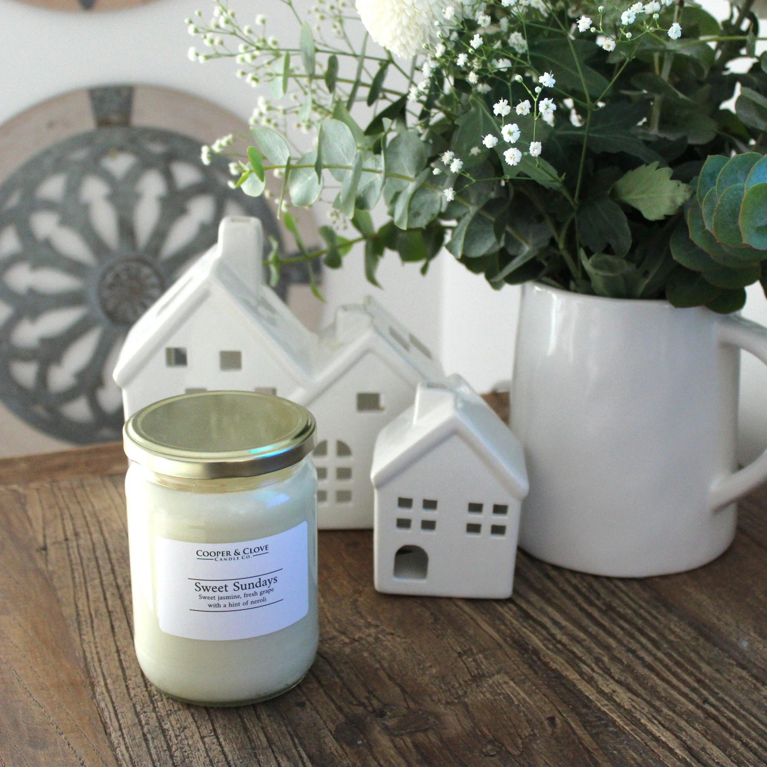 Sweet Sundays soy candle with jasmine & grape scent, styled with white ceramic houses and fresh flowers on wood